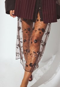 Leggings in pizzo nero trasparente con motivi floreali in paillettes, abbinati a un blazer oversized a righe bordeaux.