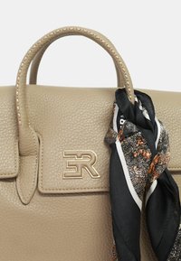 Borsa in pelle beige con forma strutturata, caratterizzata da un logo dorato, manici cuciti e una sciarpa nera con motivo annodata attorno al manico.