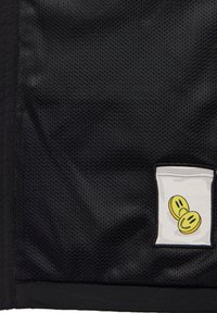 Black mesh fabric featuring a white patch with a bag design and two yellow smiley faces. Text on the patch reads “SWEET,” and “SOUR."