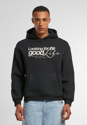Sweatshirt à capuche noir en matériau doux, avec une poche avant et un texte blanc audacieux disant "À la recherche de la belle vie."