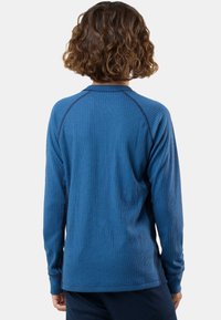 Person with curly brown hair wearing a blue long-sleeve ribbed shirt shown from the back against a plain light background.