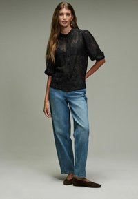 Schwarze Spitzenbluse mit Knöpfen und Puffärmeln, kombiniert mit hellblauen geraden Jeans und braunen Schuhen. Einfaches Design und strukturiertes Material.