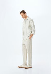 Lässiges Outfit mit einem hell gestreiften Button-Up-Hemd, beigen weiten Hosen und weißen Sneakers mit braunen Akzenten.