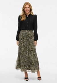 Must have musta varrukatega blus, millel on vertikaalne tekstuur, koos pika, voolava leopardimustriga seeliku, mille värvid on pruunid ja beežid. Mustad plokk-kontsad.