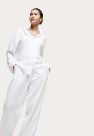 Witte textuur pyjamaset met een knoopsluiting shirt met kraag en losse broek met zakken en drawstring taille.