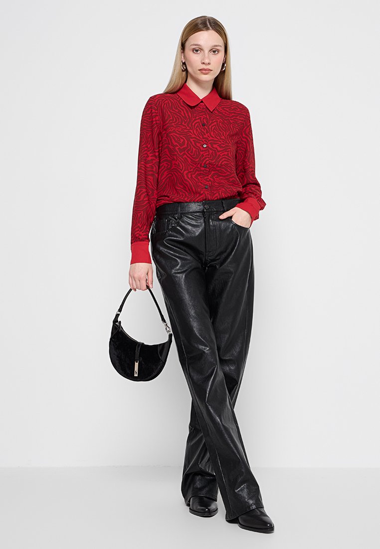 Blouse rouge à motifs avec un col, pantalon large en cuir noir, et un petit sac à main noir, associés avec des chaussures à talons noires.