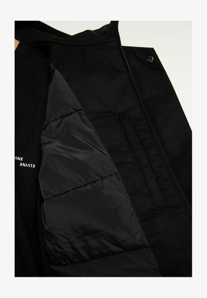 Schwarze Jacke mit Innenfutter, das gesteppt ist, einer glatten Textur und verdeckten Taschen. Das Design umfasst einen Reißverschluss und einen Druckknopfverschluss.
