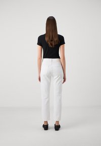 Camiseta ajustada negra, vaqueros blancos de talle alto con bolsillos traseros, corte de pierna recta, combinados con zapatos de tacón negros, fondo minimalista.