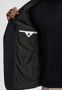 Granatowa marynarka z czarną, paskowaną podszewką, z kieszenią obszytą białą lamówką i pojedynczym zapięciem na guzik. Miękki, fakturowany materiał.