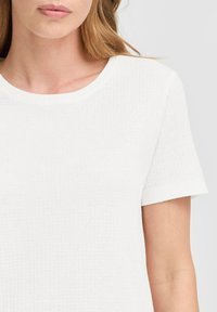 T-shirt bianco a maniche corte con un design a coste testurizzato e scollatura arrotondata, che mette in evidenza un tessuto liscio e una forma attillata.