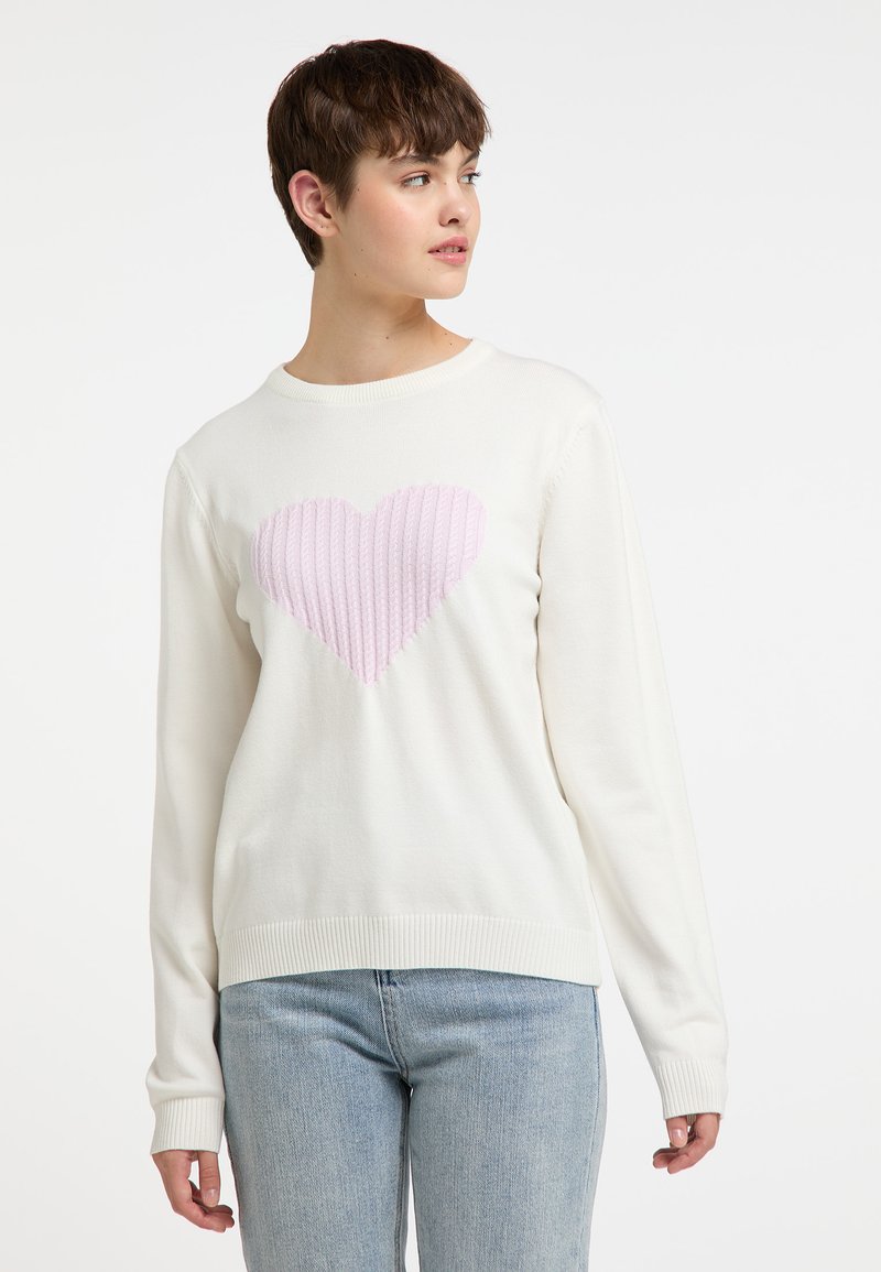 Pull en blanc avec un motif de cœur rose pastel côtelé au centre. Présente un col rond et des poignets côtelés, fabriqué dans un matériau en tricot doux.