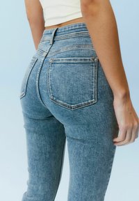 Blå denimjeans med en tætsiddende pasform, der har en mid-rise talje, to baglommer og synlige sømdetaljer.