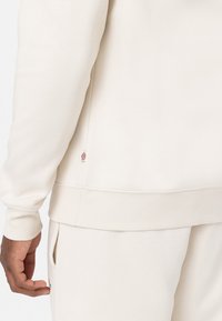 Beige sweatshirt van zacht stof, met ribbels aan de mouwen en onderkant, een klein logo-label aan de zijkant en een relaxte fit.
