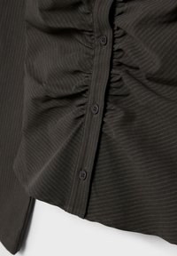 Tessuto scuro a righe sottili con dettaglio arricciato e una fila di bottoni neri lungo la cucitura centrale di un capo di abbigliamento.