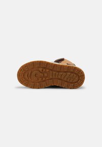 Sola de bota de borracha castanha com padrões de sulcos profundos; apresenta uma forma plana e arredondada, com superfície texturizada para maior tração. Marca visível.