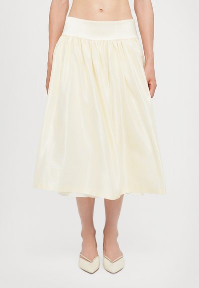 Falda color crema hasta la rodilla con cintura fruncida, hecha de tela suave, que presenta una cinta ancha en la cintura y un brillo sutil.