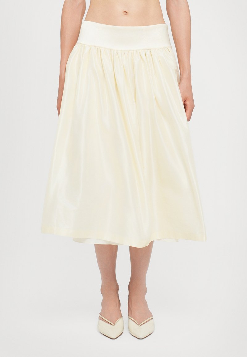 Falda color crema hasta la rodilla con cintura fruncida, hecha de tela suave, que presenta una cinta ancha en la cintura y un brillo sutil.