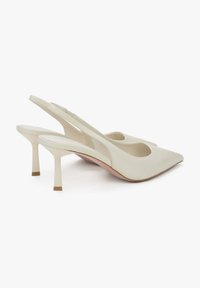 Kremowe buty type slingback z szpiczastym noskiem, górą z gładkiej skóry i cienkim, wysokim obcasem. Posiadają wycięty design i minimalistyczny styl.