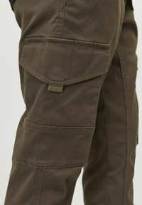 Cargo nohavice v tmavo olivovej farbe, s viacerými vreckami, odolnou bavlnenou zmesou a viditeľnými detailmi šitia.