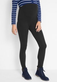 Leggings noires taille haute en tissu extensible, associés à des bottines lacées bleu marine. Le haut présente des rayures blanches horizontales.