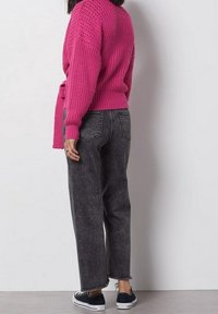 Ljust rosa stickad tröja med ribbad nederkant, kombinerad med mörkgrå jeans med hög midja som har fransade ärmslut och blå sneakers.