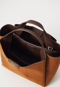 Brun semsketotebag med lærhåndtak, innvendig glidelåslomme og kontrasterende sømmer. Romslig design med strukturert form.
