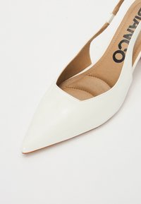 White slingback shoe with a pointed toe, smooth leather exterior, and a tan insole. Features a cut-out design and minimalistic look.