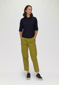 Niebieska, fakturowana, kapturowa bluzka z krótkimi rękawami, w zestawieniu z oliwkowymi spodniami z bocznymi kieszeniami i zwężanym krojem. Uzupełniona ciemnymi trampkami.