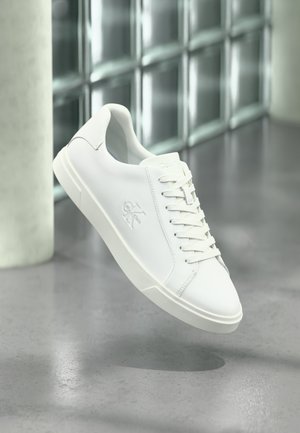 Hvit skinnsneaker med glatt finish, snøresystem, logodetalj på siden og en kontrasterende hvit gummisåle.