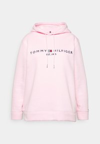 Vaaleanpunainen huppari, joka on tehty pehmeästä kankaasta ja jossa on keskellä laivastonsinisellä teksti "TOMMY HILFIGER EST. 1985" oleva logo.