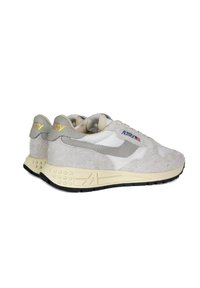 Sneaker con una combinazione di suede grigio chiaro e pelle bianca, con suola in gomma crema e dettagli gialli sul tallone e sul logo del marchio.