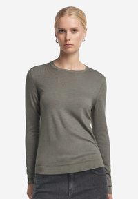 Olivgrüner Pullover mit langen Ärmeln, rundem Halsausschnitt, feiner Strickstruktur sowie gerippten Bündchen und Saum, kombiniert mit dunkler Jeans.