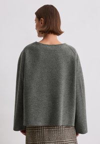 Grijze wollen pullover met een brede halslijn en verlaagde schouders, gecombineerd met een bruine en beige gestreepte rok. Gestructureerde stof.