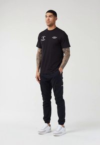 Musta puuvillainen t-paita, jossa valkoiset graafiset painatukset, yhdistetty laivastonsinisiin cargo-housuihin, joissa on vetoketjutaskut, ja valkoisiin lenkkareihin. Sileä pinta.