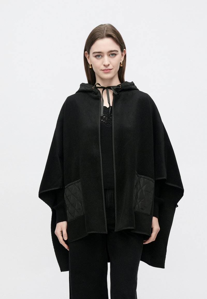 Mustast pehmest kangast kapuutsiga viig, millel on tikitud küljetaskud, lukuga sulgemine ja dekoratiivne lips kaeluse juures.