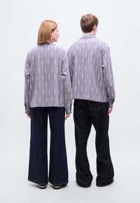 Γκρι μακρυμάνικα πουκάμισα με μοτίβο, συνδυασμένα με φαρδιά παντελόνια από σκούρο τζιν. Και τα δύο πουκάμισα έχουν άνετη εφαρμογή και πλαϊνές σχισμές.