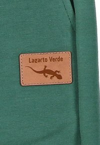 Groene katoenen kleding met een rechthoekige bruine leren patch met het label "Lagarto Verde" en een hagedisgrafiek met stikseldetail.
