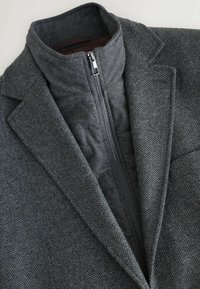 Giacca con motivo houndstooth grigio e colletto alto, con zip nascosta e fodera interna a contrasto in grigio uniforme.