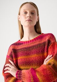Brede trui met een ronde halslijn, versierd met horizontale strepen in roze, oranje en rood. Dikke, getextureerde garen met geribbelde manchetten.
