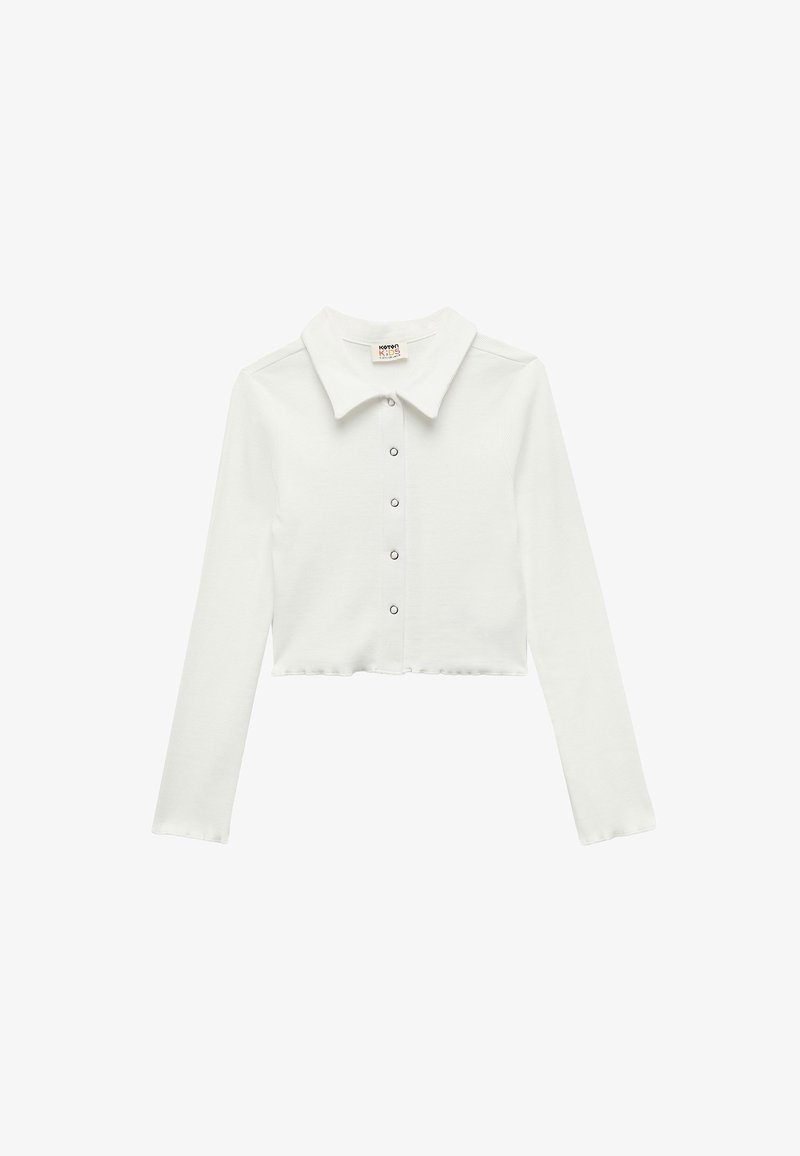 Chemise blanche courte à manches longues avec col pointu et cinq boutons-pression sur le devant, en tissu côtelé.