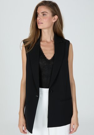 Black sleeveless blazer made of a smooth fabric, featuring a tailored design, sharp lapels, a single button closure, and side pockets.