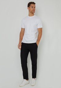 Camiseta de algodón blanca de manga corta, combinada con pantalones negros y zapatillas blancas. El conjunto presenta un diseño casual y estilizado.