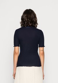 Haut en maille côtelée navy à manches courtes, bords festonnés, design ajusté et tissu texturé, associé à une jupe plissée de couleur claire.