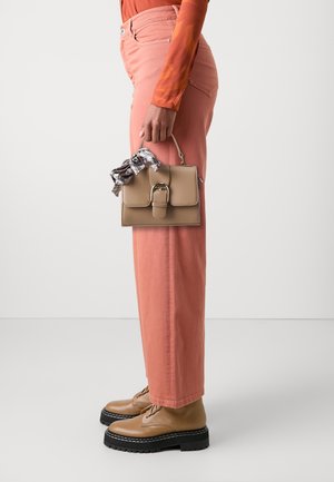 Beige håndtaske med en top-håndtag, der har en sølvspænde og et ternet tørklæde som accent. Sammen med pink brede bukser og tan snørebåndssko.