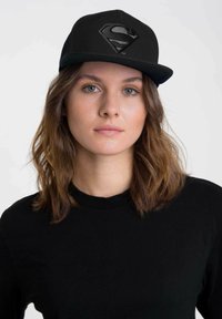 Schwarze Kappe mit einem erhabenen, gestickten Superman-Logo in Schwarz auf der Vorderseite. Die Kappe hat einen flachen Schirm und einen klassischen Snapback-Stil.