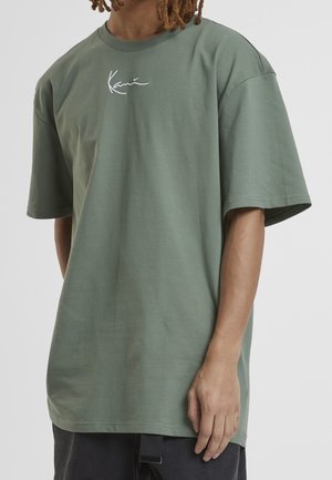 Grøn bomulds t-shirt med korte ærmer, der har et hvidt broderet logo på brystet. Ret snit og glat tekstur.