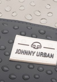 Black and gray waterproof bag with raised dots. Features a white label with "JOHNNY URBAN" text. Textured surface and water droplets visible.