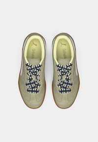 Chaussures de sport beiges avec un dessus texturé, des lacets à motifs bleu marine et une semelle en caoutchouc. Elles présentent des semelles intérieures jaunes douces avec le logo de la marque.