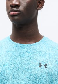 Αθλητική μπλούζα σε ανοιχτό μπλε χρώμα με υφασμάτινο μοτίβο, στρογγυλή λαιμόκοψη και μαύρο λογότυπο Under Armour στο αριστερό μέρος του στήθους.