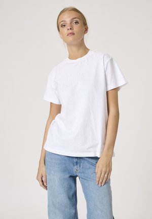 Hvid bomulds t-shirt med korte ærmer, rund hals og subtilt prikkemønster. Sammen med lyseblå denim jeans i afslappet pasform.
